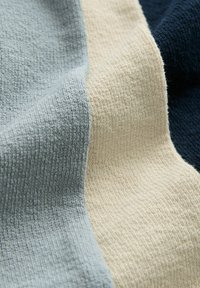 Tissu texturé dans des couleurs douces : bleu clair, crème et marine. Présente une surface côtelée avec des tissages variés et une sensation de confort.