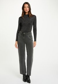 Maglietta nera a costine a maniche lunghe abbinata a jeans dritti grigi a vita alta. Outfit completato da stivali neri alla caviglia.