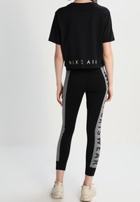 Černé zkrácené tričko s bílým nápisem "NIKE AIR" na zádech; v kombinaci s černými legínami s šedými bočními panely a textem "SPORTSWEAR".