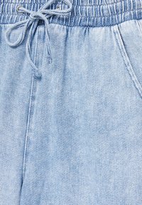 Joggers de mezclilla azul claro con cinturilla elástica, cierre de cordón y bolsillos laterales. La tela tiene una apariencia suave y texturizada.