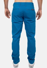 Helderblauwe katoenen broek met een slim fit, voorzien van rode stiksels, achterzakken en omgeslagen manchetten. Merklabel zichtbaar aan de achterkant.