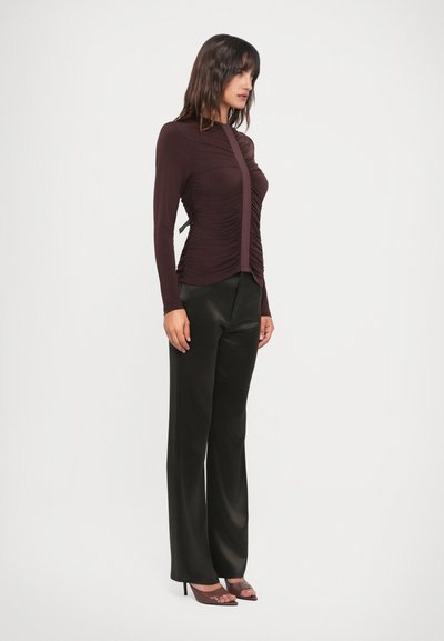 Burgundy long-sleeve top with ruching detail and side ties paired with shiny black wide-leg trousers and strappy heeled sandals.