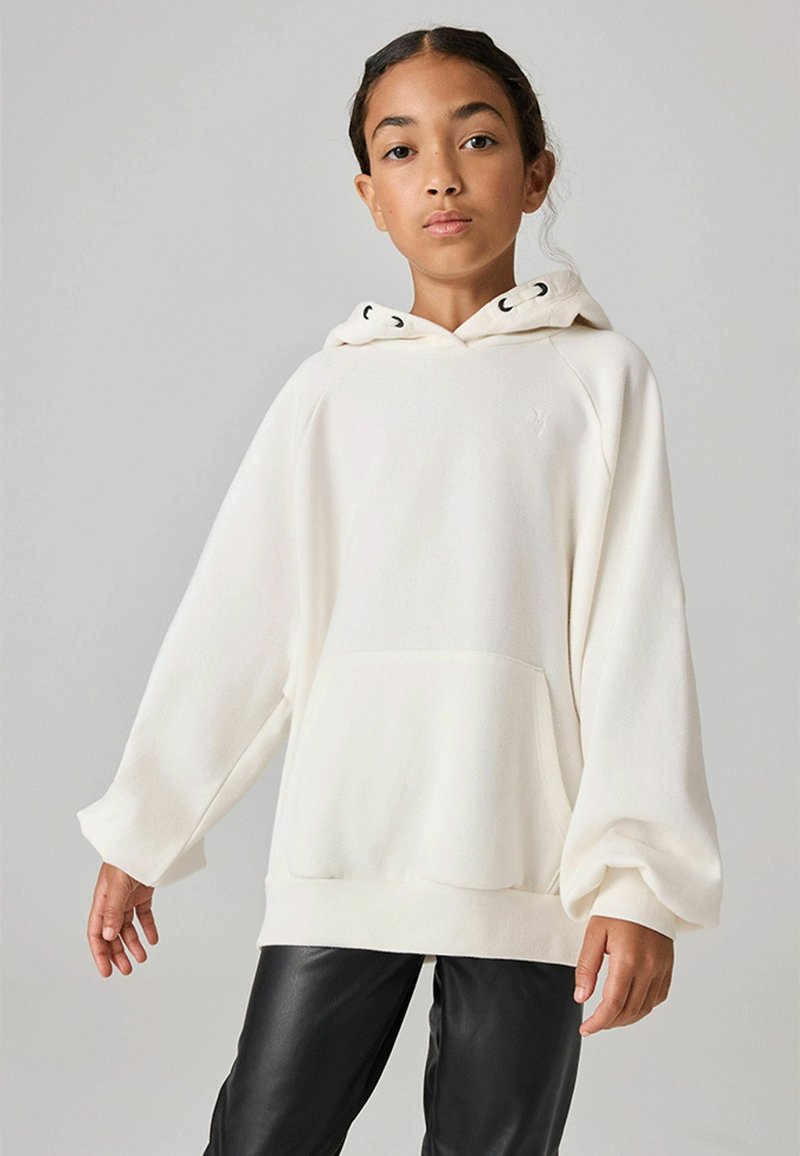 Hoodie bianco oversize realizzato in tessuto morbido, con tasca a canguro, cappuccio con coulisse e polsini a costine. Abbinato a pantaloni neri in pelle.