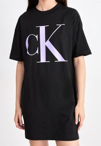 Czarna sukienka z bawełny w fasonie t-shirta, z dużym lawendowym logo "CK" z przodu. Krótkie rękawy i luźny krój.