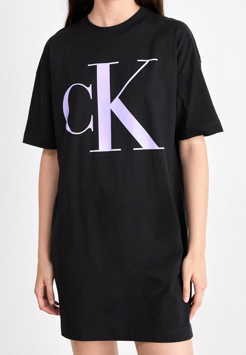 Czarna sukienka z bawełny w fasonie t-shirta, z dużym lawendowym logo "CK" z przodu. Krótkie rękawy i luźny krój.