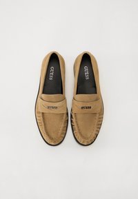 Tan semskede loafers med rund tå, dekorativ søm, mokkasinstil, GUESS-logo på forsiden og svart såle.