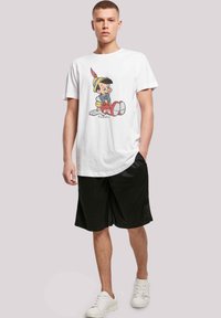 Hvit bomulls t-skjorte med et fargerikt Pinocchio-motiv, kombinert med svarte shorts og hvite sneakers. Ledig passform med rund utrigning.