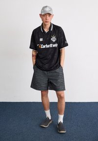 Fekete sportmez fehér gallérral és logóval, csíkos szürke rövidnadrággal párosítva. Szürke sapka és szürke sportcipő, kiegészítve díszítésekkel.