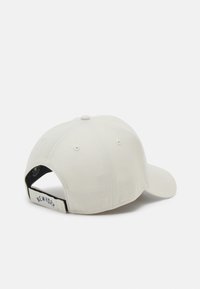 Casquette de baseball de couleur claire avec une visière courbée, en coton. Présente des trous de ventilation cousus et une étiquette "NEW YORK" à l'arrière.