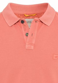 Koralfarvet polo shirt lavet af struktureret bomuld, med en klassisk krave, to sorte knapper, og et lille logo på kanten.