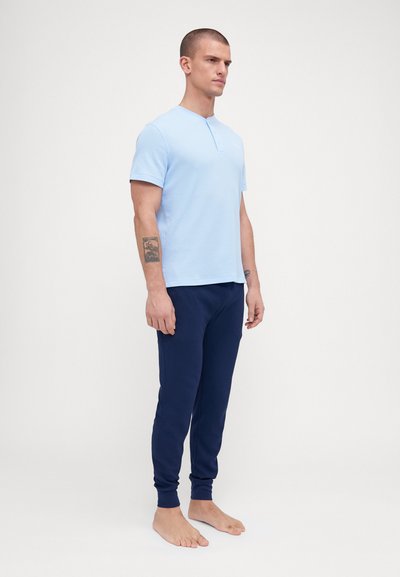Polo-shirt bleu clair à manches courtes avec patte de boutonnage, associé à un pantalon bleu marine. Le tissu semble lisse et légèrement texturé.