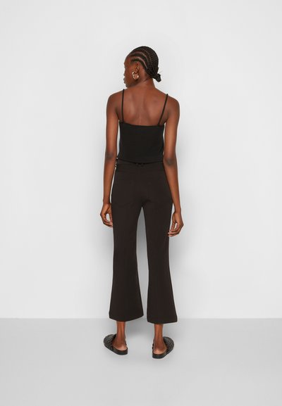 Top de malha preto com alças finas, combinado com calças pretas de boca de sino, sandálias texturizadas e brincos de argola minimalistas.