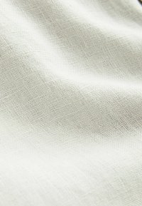 Textureret lysbeige stof med et subtilt vævemønster, der viser bløde draperinger og bløde folder.