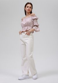 Haut rose clair à pois, décolleté épaule dénudée avec des manches volantes, associé à un jean blanc à jambes larges et des baskets blanches. Design simple et décontracté.