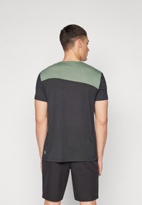 T-shirt nera con pannello verde sulle spalle, maniche corte, colletto rotondo, con un piccolo accento del marchio sul lato. Tessuto morbido.