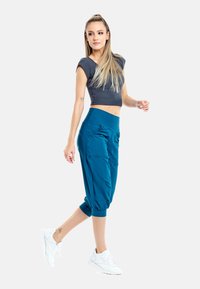 Top corto gris con mangas cortas y pantalones azules ajustados con bolsillos laterales. La modelo lleva zapatillas blancas, con un ajuste suave y relajado.