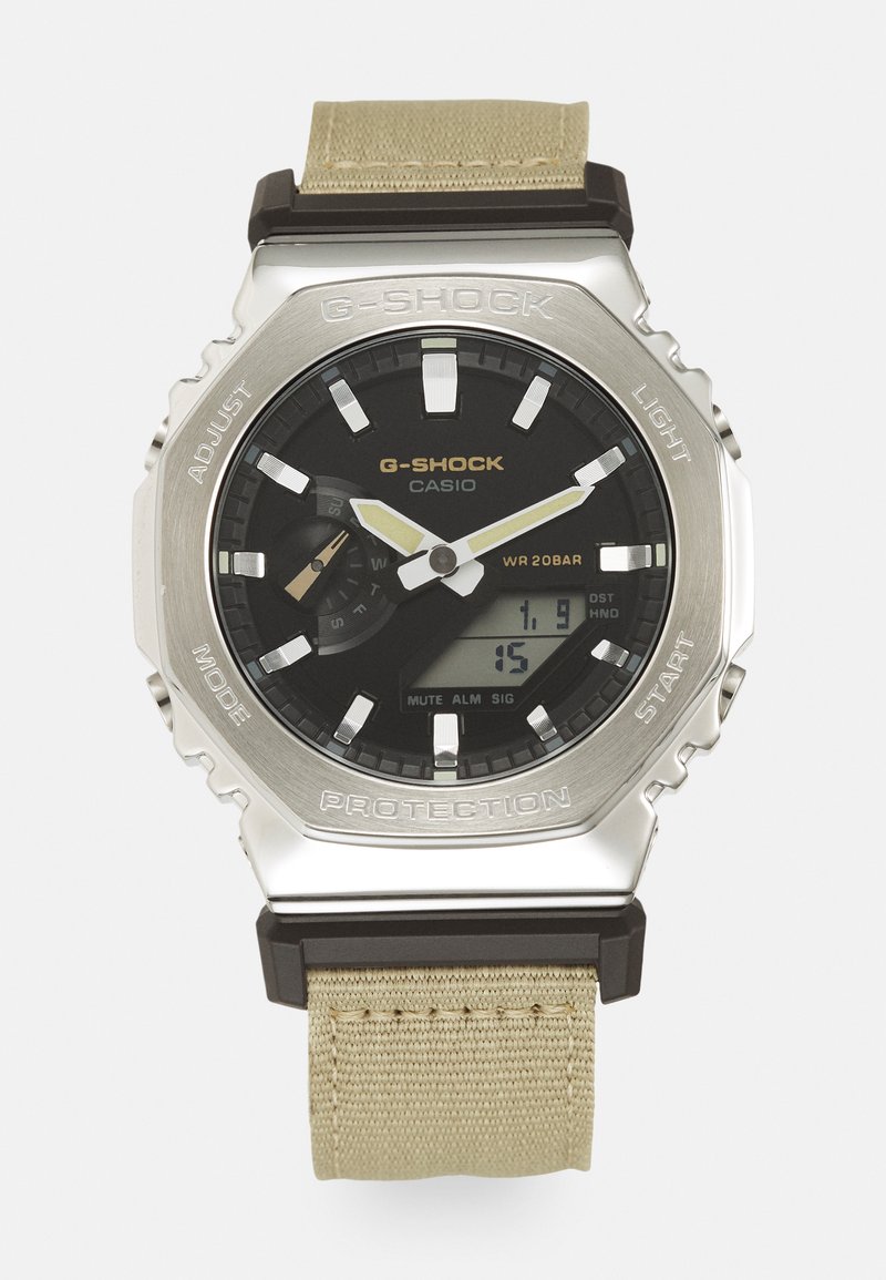 G-Shock kell hõbedasest roostevabast terasest korpusega, musta koonus, valgete ja kuldsete aktsentidega ning beežist kangastrapiga; veekindel kuni 20 baari.
