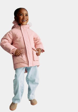 Pink puffy jacket with a hood and faux fur trim, featuring side pockets. Worn with light blue jeans and tan shoes. Smiling child.