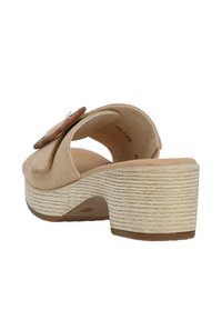 Beige suede heeled sandals featuring a curved design, textured wedge sole, and a decorative wooden button accent on the side.