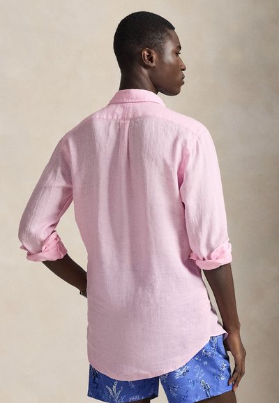 Ροζ λινό πουκάμισο με μακριά μανίκια, άνετη γραμμή και γιακά με κουμπιά, συνδυασμένο με μπλε σορτς με λευκό σχέδιο.