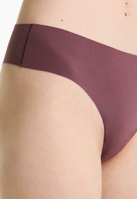 Close-up van een persoon met naadloze mauve onderkleding, met gladde stof en huid met natuurlijke kleine moedervlekken.