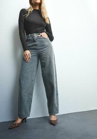 Hoog-waist, lichtblauwe denim wijde pijpen jeans met een vervaagde afwerking, gecombineerd met puntige schoenen met luipaardprint en een zwarte fitted top met lange mouwen.