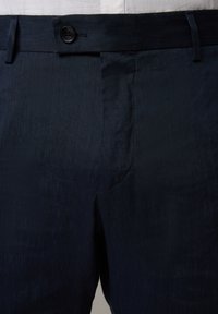 Marinblå linbyxor med en slät textur, på pricken med en enkel knappstängning och bälteloopar, skräddarsydd passform och en subtil glans.