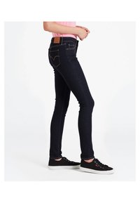 Jeans de mezclilla azul oscuro con un corte ajustado, que cuentan con costuras contrastantes, un parche de cuero en la cintura trasera y bolsillos traseros con detalle de emblema.