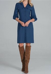 Navyblaues Knopfkleid mit Kragen, zwei Brusttaschen und Dreiviertelärmeln; kombiniert mit knielangen braunen Wildlederstiefeln.