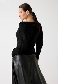 Maglione nero testurizzato con scollo rotondo e design a maglia aperta, abbinato a una gonna in pelle nera lucida con una finitura liscia.
