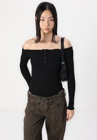 Juoda of-the-shoulder ilgos rankovės palaidinė su mygtukų detalėmis, derinama su rudomis leopardų rašto džinsais. Modelis laiko mažą juodą rankinę.