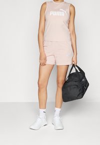 Rosa ärmlös top med vit "PUMA"-logotyp, matchande rosa shorts, vita träningsskor och en svart sportväska med svarta remmar.