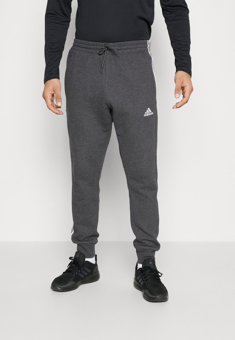 Sive hlače s elastiko in vrvico za zategovanje, s belimi bočnimi črtami in logotipom Adidas na levem stegnu.