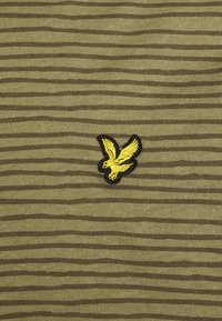 Olivově zelená látka s horizontálními pruhy, uprostřed s černou a žlutou vyšívanou ptáčkovou logem. Měkká textura, neformální design.