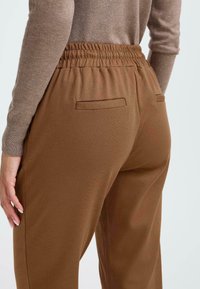 Braune Hosen mit elastischem Bund und strukturiertem Finish, ausgestattet mit zwei Gesäßtaschen und einer entspannten Passform. Mittelschweres Material.