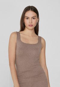 Débardeur en coton brun avec une encolure carrée, des bretelles larges et une coupe ajustée. Texture lisse sans motifs visibles ni éléments métalliques.