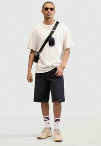 White short-sleeve t-shirt, dark denim shorts, black crossbody bag, tan sneakers, and striped socks. Accessories include sunglasses and a watch.
