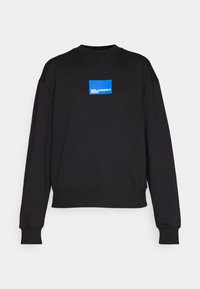 Sudadera negra con cuello redondo, con un parche de logo rectangular azul en el pecho, puños acanalados y un corte relajado.