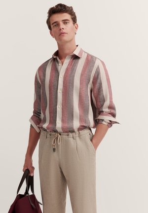 Gestreiftes Leinenhemd mit roten, cremefarbenen und grauen vertikalen Streifen, Knopfleiste vorne, aufgerollte Ärmel, kombiniert mit hellbeigen Jersey-Hosen mit Kordelzug.
