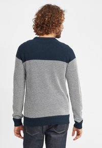 Maglione in maglia da uomo con una parte superiore blu, che si trasforma in una parte inferiore bianca texturizzata, con polsini e orlo a coste.