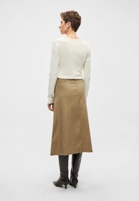 Krēmkrāsas garām piedurknēm topi, kas kopā ar bēša A-veida svārkiem un brūniem, augstpapēžu zābakiem līdz ceļiem. Gludas auduma virsmas ar smalkām šuvēm un strukturētu piegriezumu.