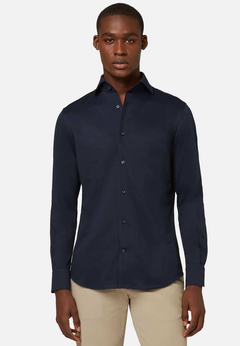 Camisa de botones de manga larga color navy, hecha de una tela suave, que presenta un cuello clásico, botones negros y un dobladillo curvado.