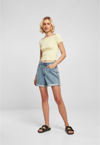 Gul kortärmad crop top i kombination med ljusblå denimshorts med upplagda fållar och svarta sandaler med spänne.