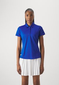 Modra polo majica s ovratnikom, kratkimi rokavi in štirimi gumbi na zapenjanju. V kompletu je off-white plisirana krila in logotip na spodnjem levem delu.