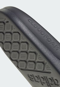 Sól sneakeru Cloudfoam v tmavosivej farbe s textúrovaným dnom, ktoré obsahuje obdĺžnikové a líniové vzory. Vyrazené "CLOUDFOAM" a "adidas".