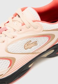 Sportovní bota broskvové a bílé barvy s prodyšným síťovinovým svrškem, zlatými akcenty a logem. Vybavena polstrovaným límcem a texturovanou podrážkou pro lepší přilnavost.