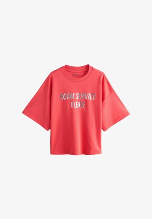 Korallszínű, rövid ujjú, bő fazonú póló ezüstszínű "ROOM SERVICE PLEASE" felirattal az elején, kerek nyakkivágással és laza szabással.