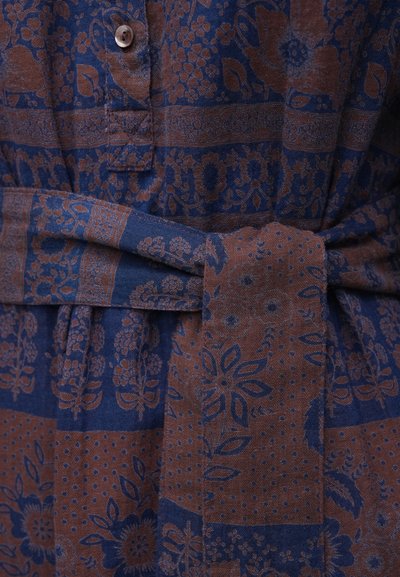 Καφέ και μπλε φόρεμα από ύφασμα με μοτίβο, εμπρόσθια κουμπιά, ζώνη με δέσιμο και λουλουδάτα σχέδια. Υφή πλέξης με πουά και γεωμετρικές λεπτομέρειες.