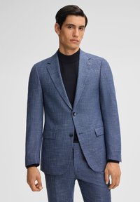 Abito blu navy su misura con un motivo tessuto testurizzato, chiusura a un bottone, rever a scanso e tasche laterali, abbinato a un dolcevita nero.