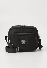 Černá nylonová kabelka přes rameno se dvěma přihrádkami na zip, vybavená stříbrnými kovovými detaily a emblémem Medusa od Versace. Součástí je nastavitelný popruh.